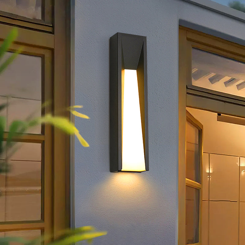 Modern outdoor LED wall light mounted on a house's exterior wall, emitting a warm white glow, highlighting its sleek design and illuminating the surrounding area.