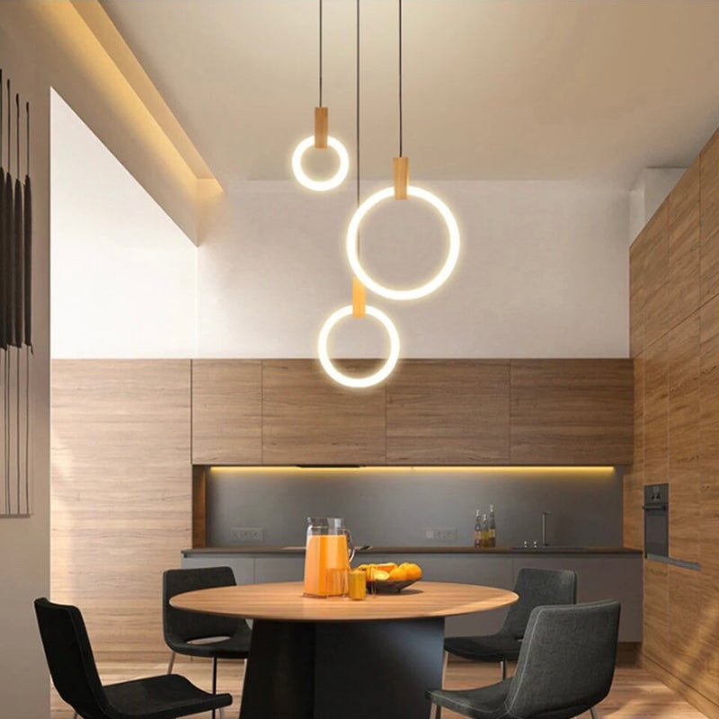 Wooden tiered chandelier with multiple LED light rings of varying sizes, elegantly suspended at different lengths above a dining table, illuminating the are with a warm, ambient glow