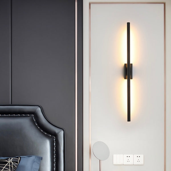 A long stick shaped wall light mounted on a wall, emitting a soft warm white glow.