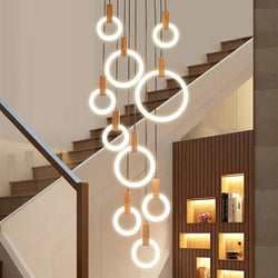 Wooden tiered chandelier with multiple LED light rings of varying sizes, elegantly suspended at different lengths above a staircase, illuminating the are with a warm, ambient glow
